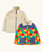 both sides of the frugi fleece jacket, one side in solid cream and one in a bright multicolor patchwork pattern with blue panels and pockets.