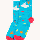 The blue sting ray socks from the Frugi pack of three sealife themed bamboo children's socks with roll tops. A blue under the ocean themed sock with sting ray, starfish, fish and coral pink coloured heel and toe caps. 