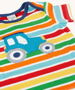 Close up of the front of the Frugi blue tractor applique rainbow striped t-shirt. Bands of red, light yellow, green, orange and light blue in-between thinner white stripes.