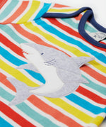 A close up of Frugi Bobster Applique T-Shirt in a Sea Rainbow Stripe print, featuring an embroidered Shark in the centre, and popper fastenings at the top.