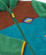 A close up of the Frugi kids braken fleece cord jacket in holly green/hotchpotch showing the diamond shaped patch on the chest and full length zip detail