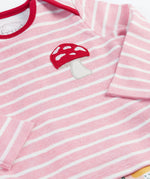 A close up of the top from the frugi kids brooke easy dressing baby grow in fun-guys/pink stripe showing the pink and white striped long sleeved top with a red mushroom applique detail on organic cotton fabric.