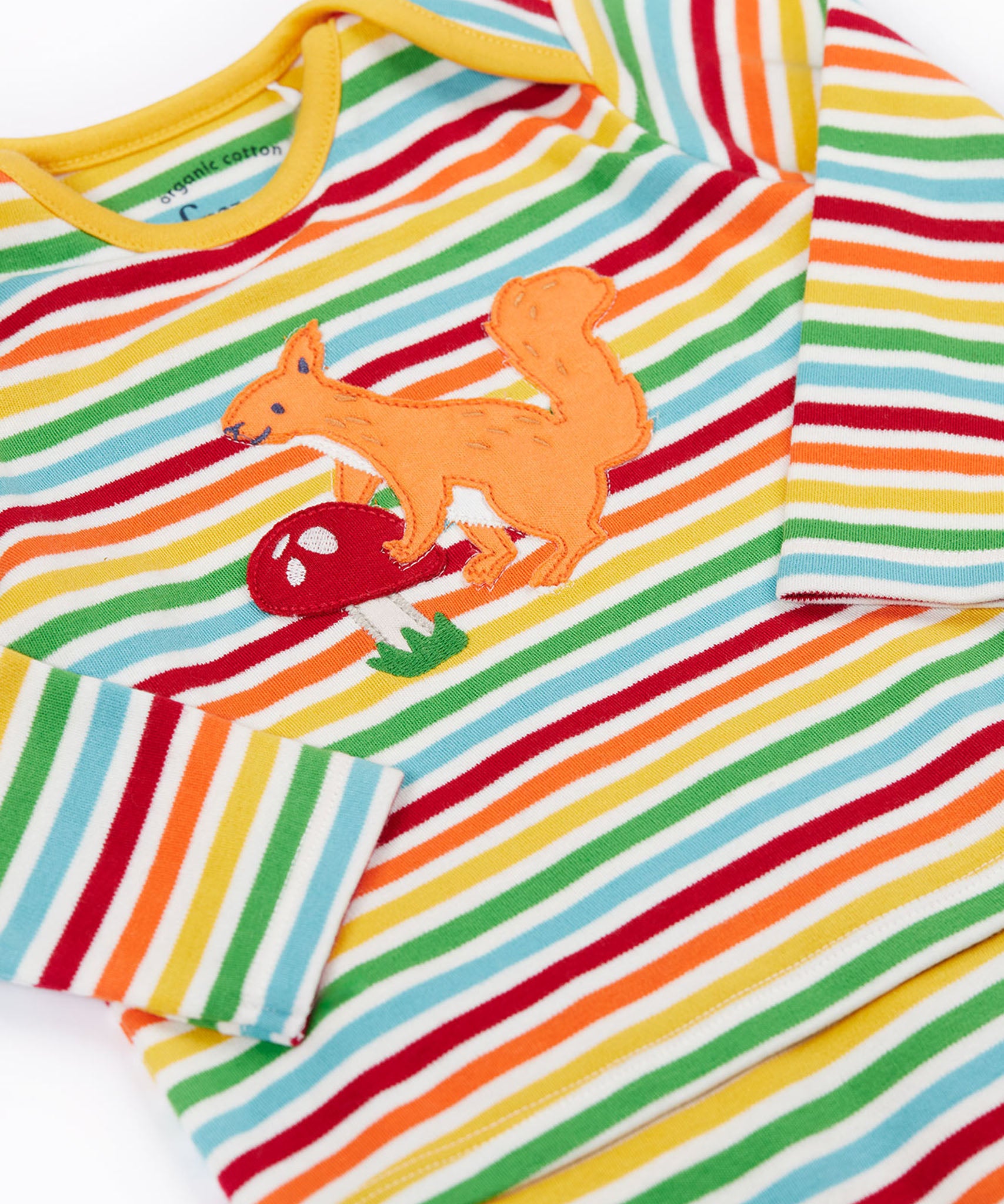 A close up of the top from the frugi kids brooke easy dressing baby grow in squirrel/rainbow stripe showing the squirrel applieque detail on rainbow striped organic cotton fabric.