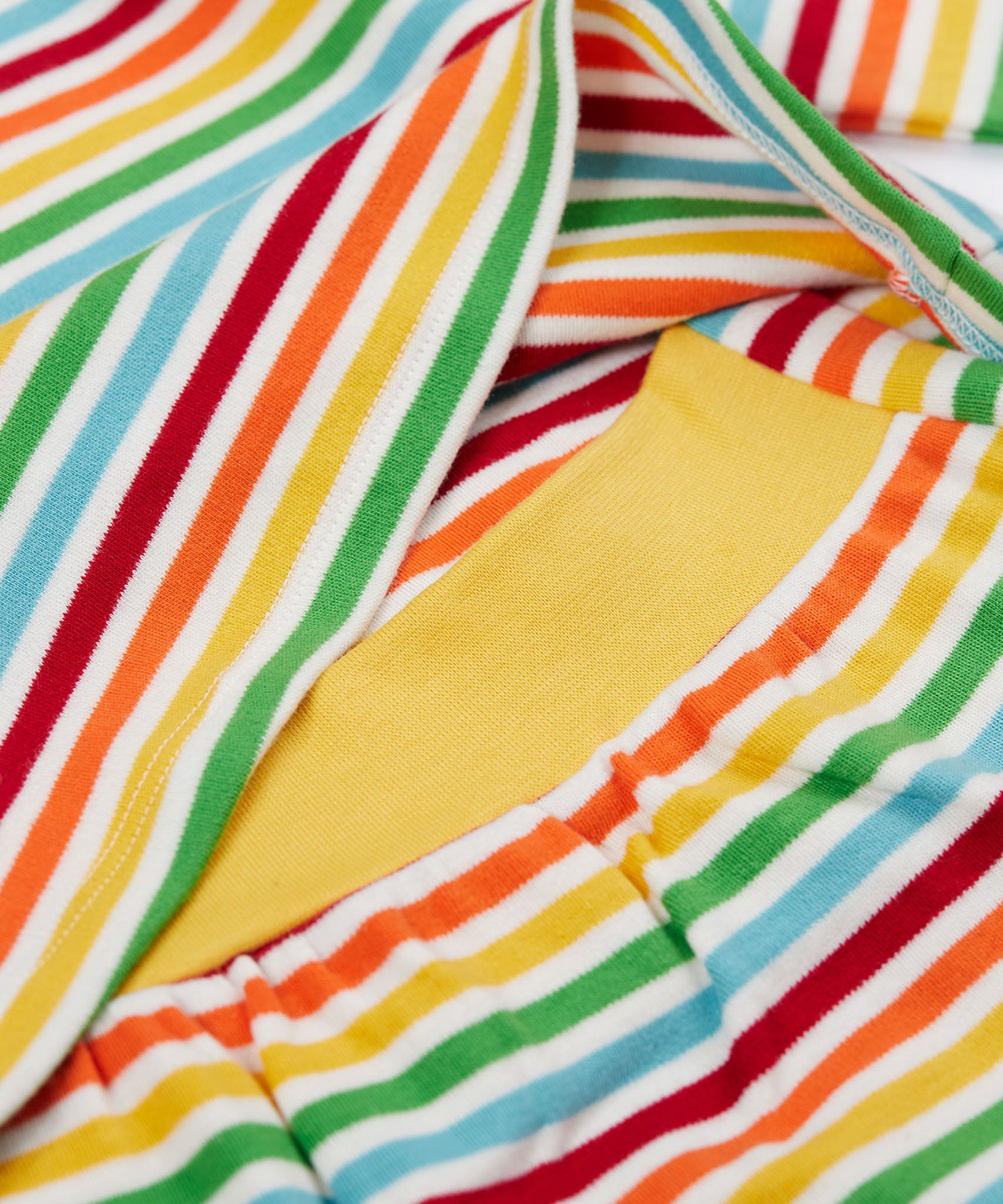A close up of the top from the frugi kids brooke easy dressing baby grow in squirrel/rainbow stripe showing the rainbow inspired striped detail and soft yellow elasticated waist band on organic cotton fabric.