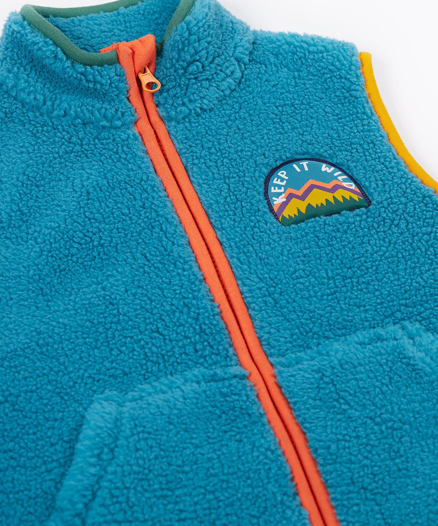 A close up of the Frugi kids bude borg fleece gilet in boat blue showing the full length zip detail on orange trim and a close up of the keep it wild patch on turquoise 100% recycled polyester material