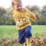 A child walking on grass wearing the Frugi Caleb Leopard Character Knit Jumper, navy cord trousers and yellow wellington boots. This knitted jumper is a part of a wide range of organic cotton clothing for children available here at Babipur. 
