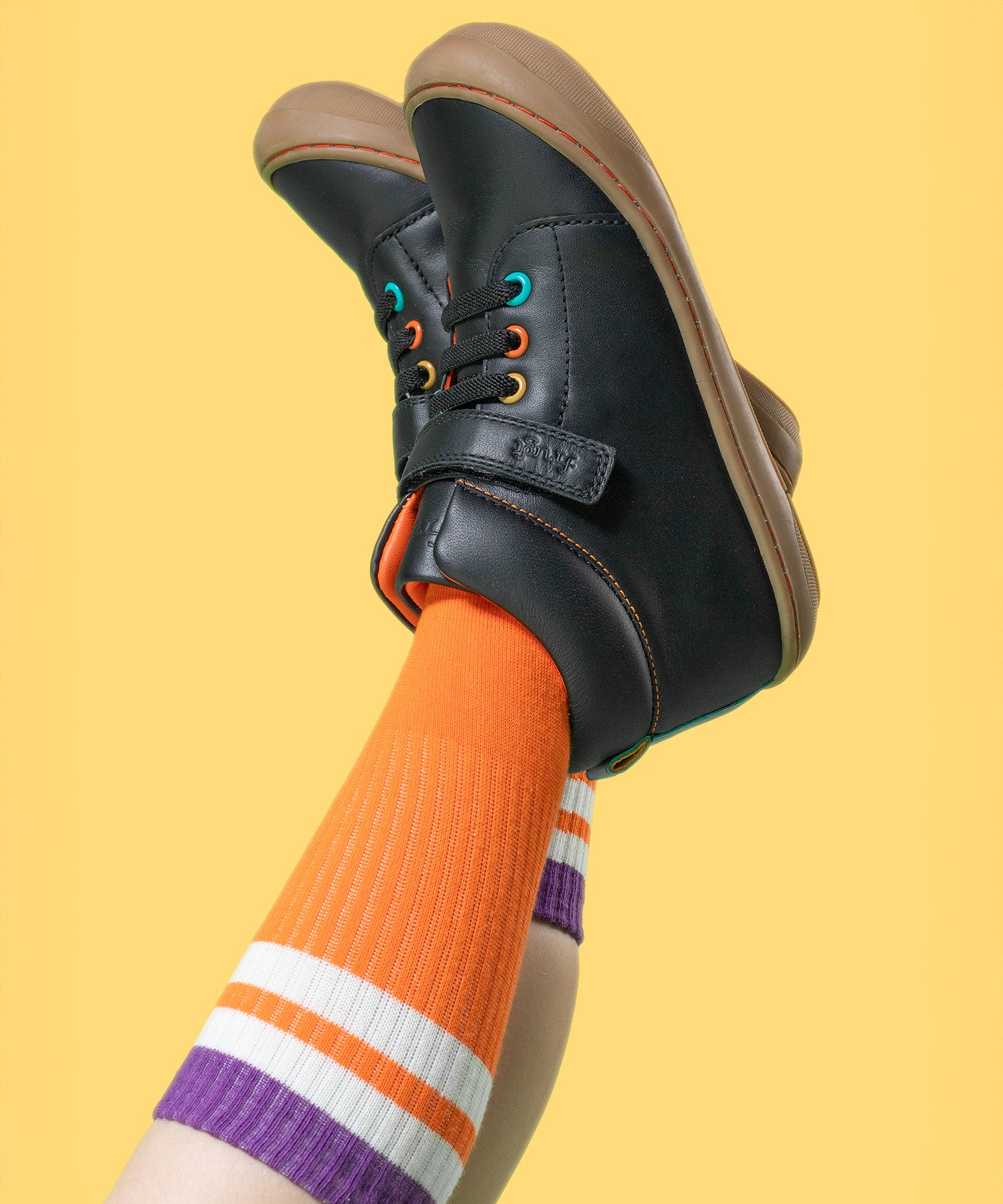 A child wearing the Frugi cape stretch children's lace boot in black leather with salamander orange leather lining. 