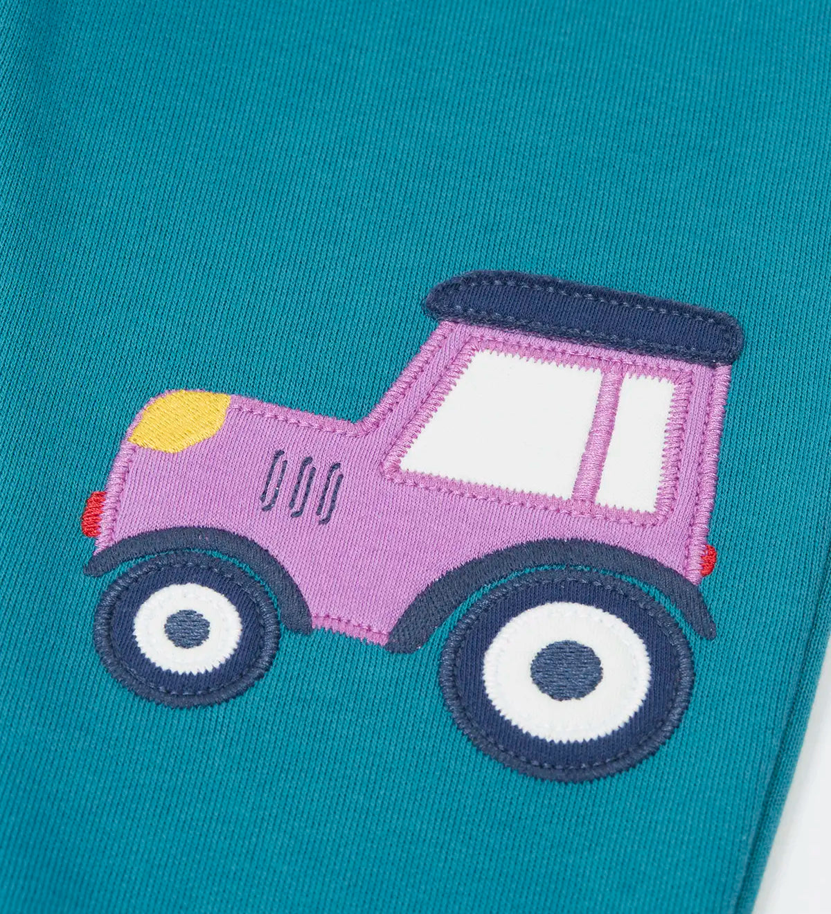 Close up of the purple tractor applique on one side of the Frugi  character joggers in boat blue.