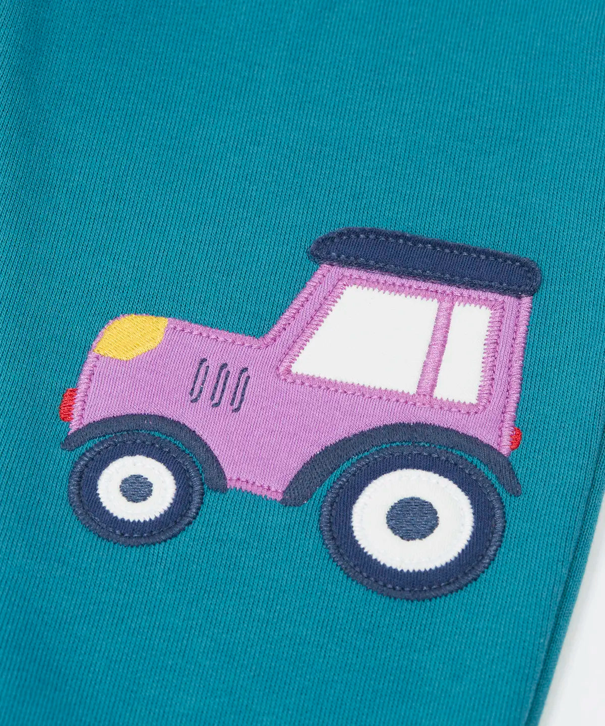 Close up of the purple tractor applique on one side of the Frugi  character joggers in boat blue.