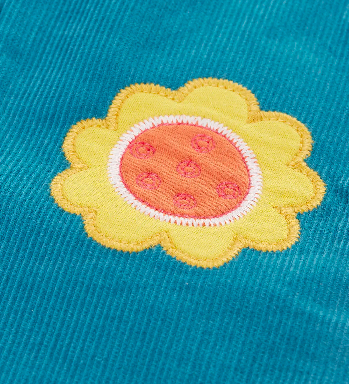 Close up of a yellow flower applique badge on the Frugi cherry boat blue corduroy flared trousers.