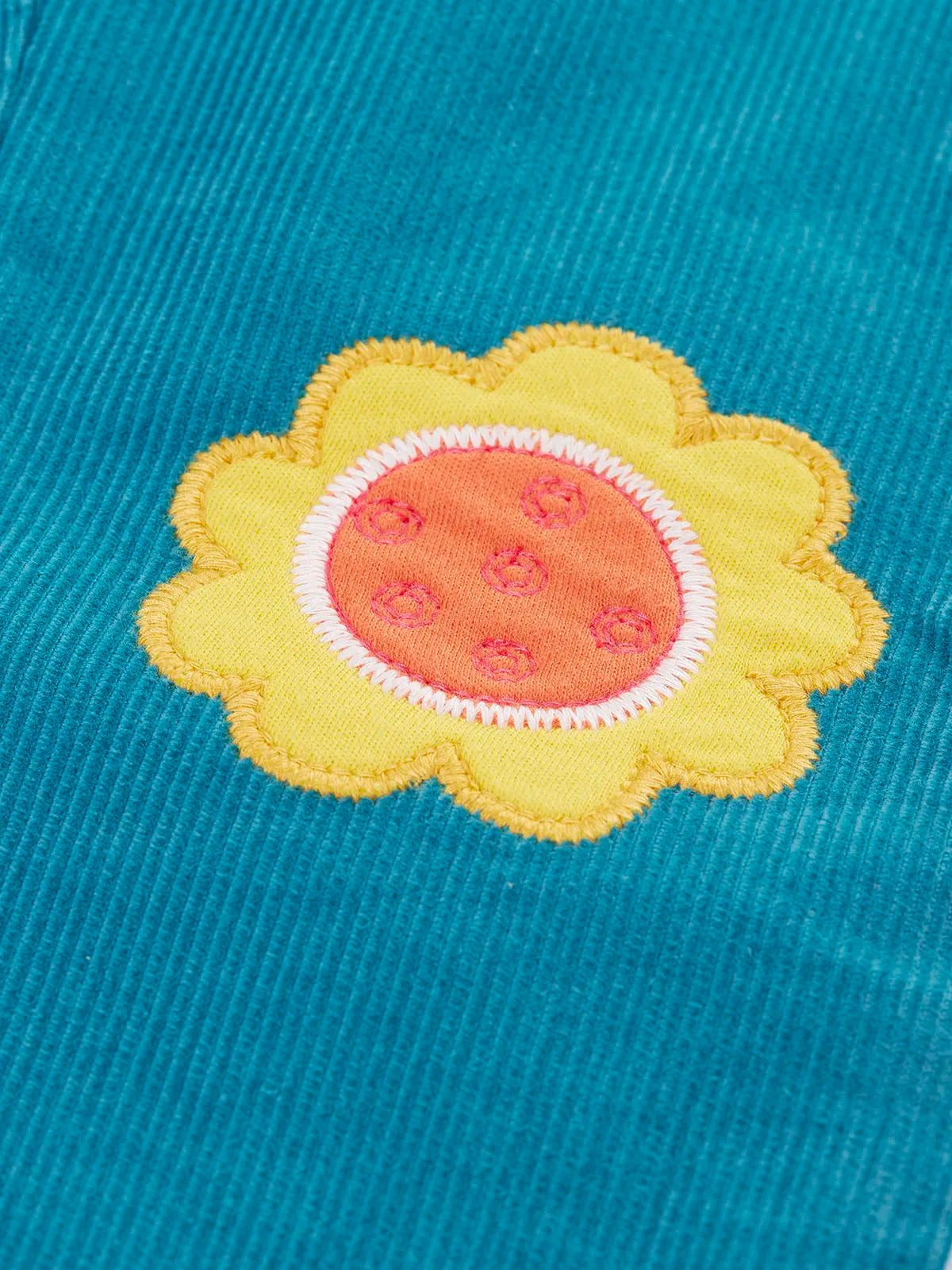 Close up of a yellow flower applique badge on the Frugi cherry boat blue corduroy flared trousers.