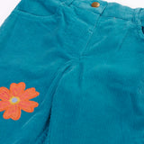 Close up of the Frugi cherry boat blue corduroy flared trousers with two flowers and a rainbow badge stye details. 