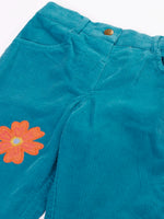 Close up of the Frugi cherry boat blue corduroy flared trousers with two flowers and a rainbow badge stye details. 