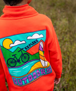 Back of Frugi Half Zip Organic Cotton Papaya orange Jumper with large Outdoors colour block style graphic. A large square filled with an outdoor scene featuring a surfboard, bike, water, mountains and sun with the word outdoors written in bold font.