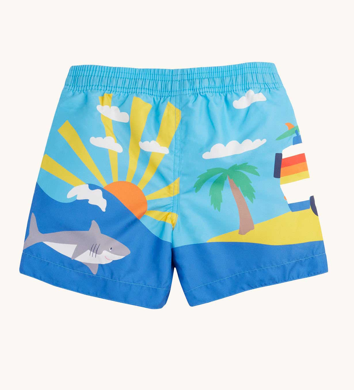 Back of Frugi blue skies beach kids board shorts. A wrap around beach scene featuring a shark, palm tree and sun.
