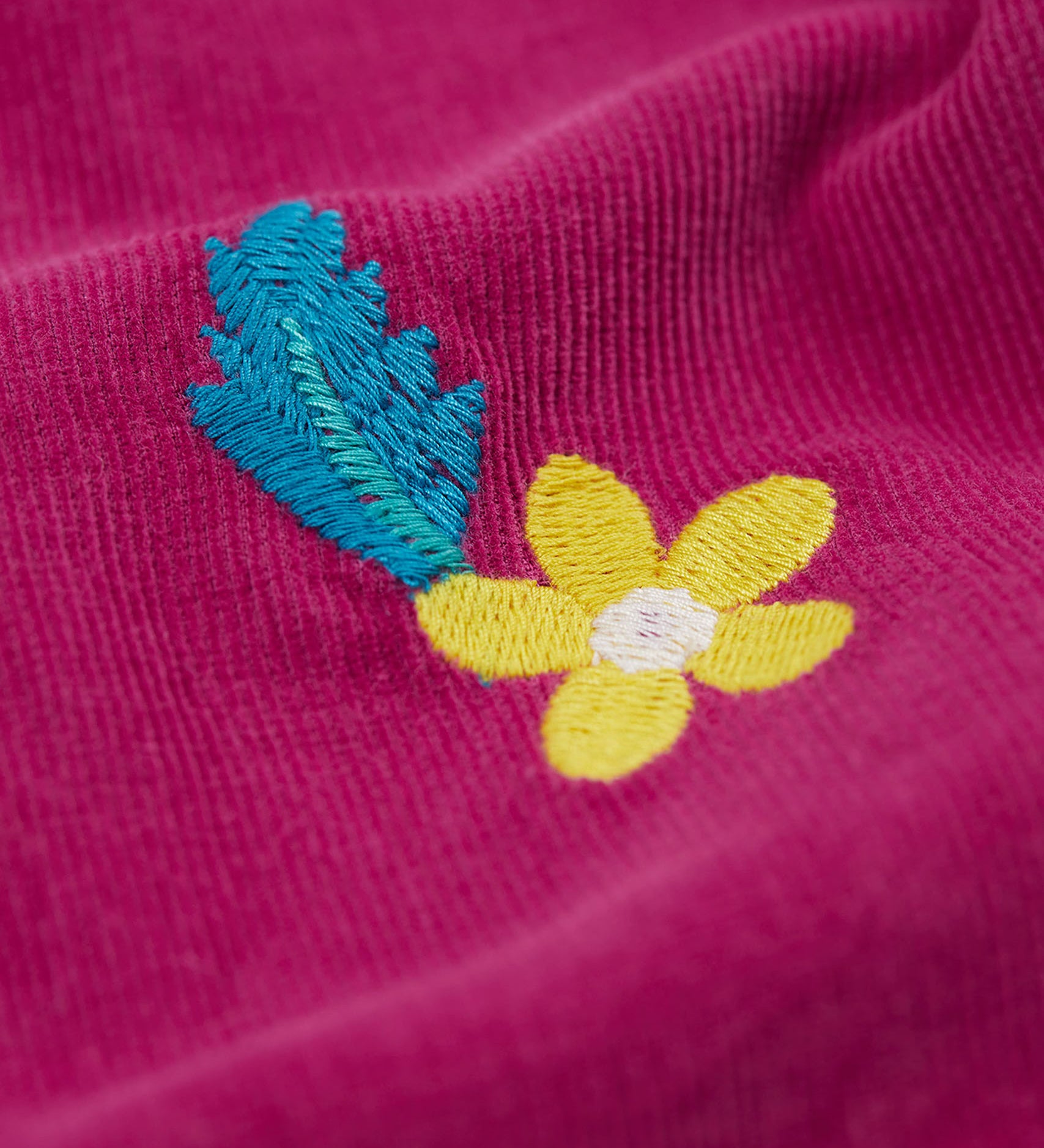 A close up of the yellow embrodered flower detail on the Frugi children's callie paperbag style with a damson colour and flora design. 