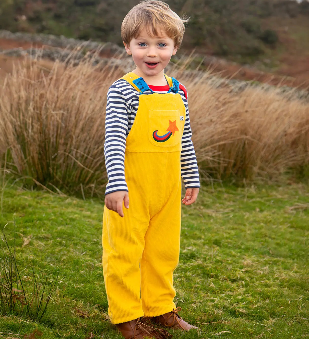Child wearing the Frugi Gylly cord reversible dungaree in bumblebee yellow with star pocket design.