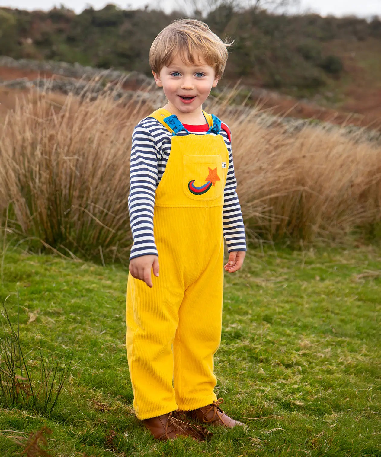 Child wearing the Frugi Gylly cord reversible dungaree in bumblebee yellow with star pocket design.