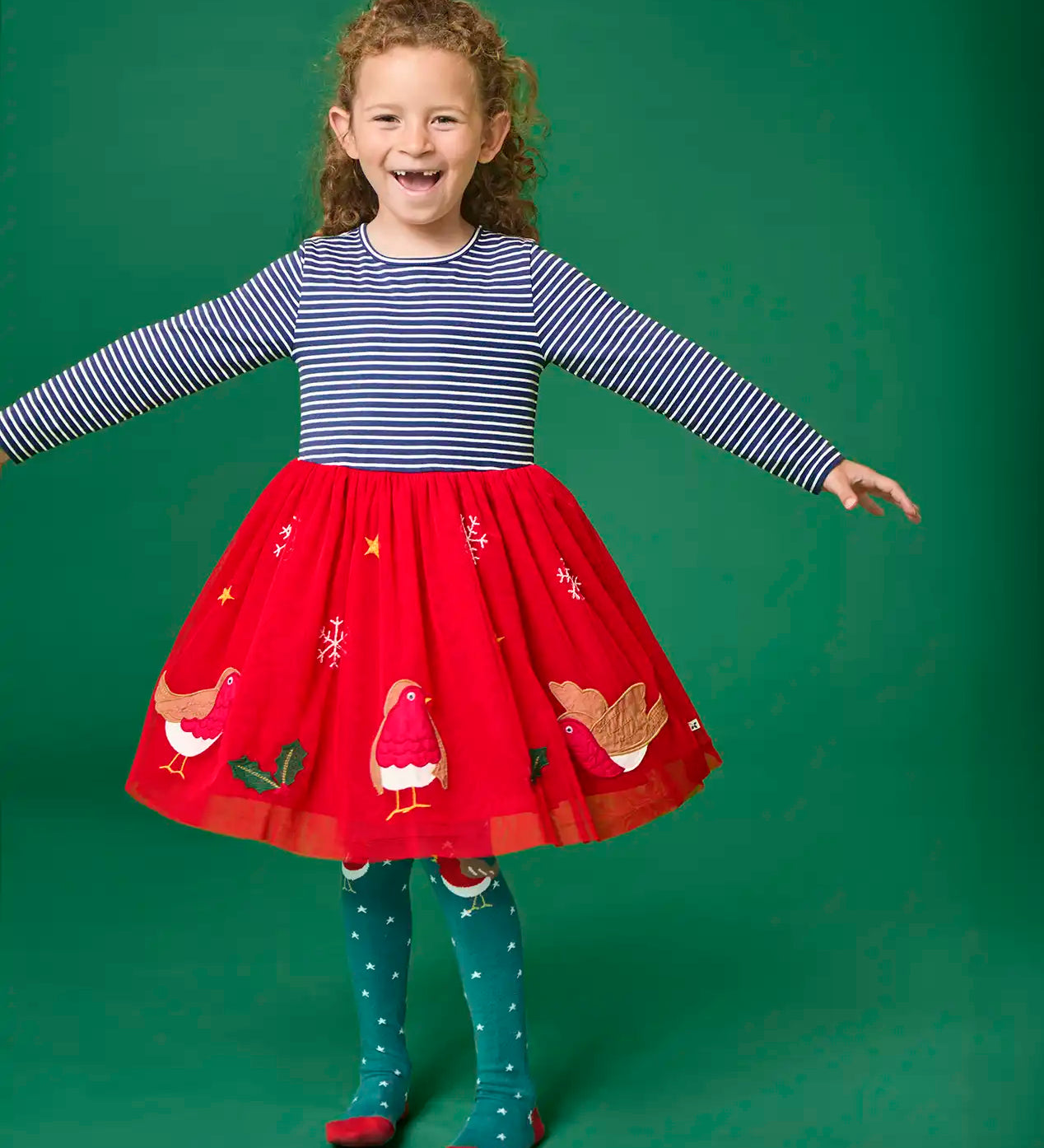 Child wearing the Frugi emmie skater dress with a long sleeved navy stripe top half and red robin applique skirt twirling around.
