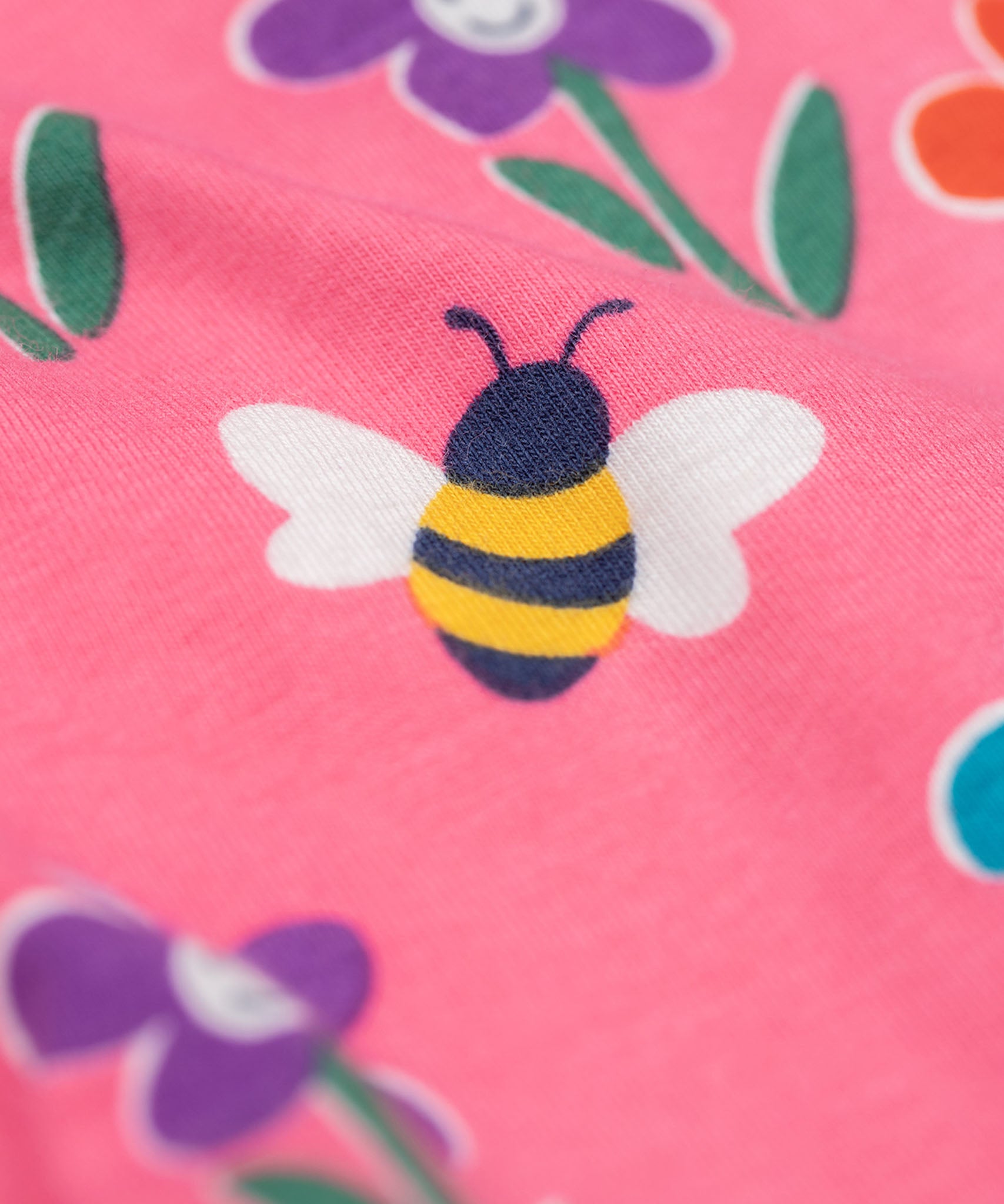 A close up of the bee on the Frugi organic cotton kids Libby leggings with a fun flowers print on a pink background.