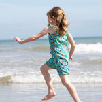 A child facing away fro,m teh camera splashing around in teh sea wearing a Frugi Children's Maris Playsuit with a  Sea Life print.