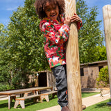 Child wearing Frugi waterproof puddle buster coat in pink purrfect ponies print, standing on a platform in a playground.