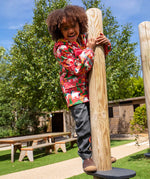 Child wearing Frugi waterproof puddle buster coat in pink purrfect ponies print, standing on a platform in a playground.