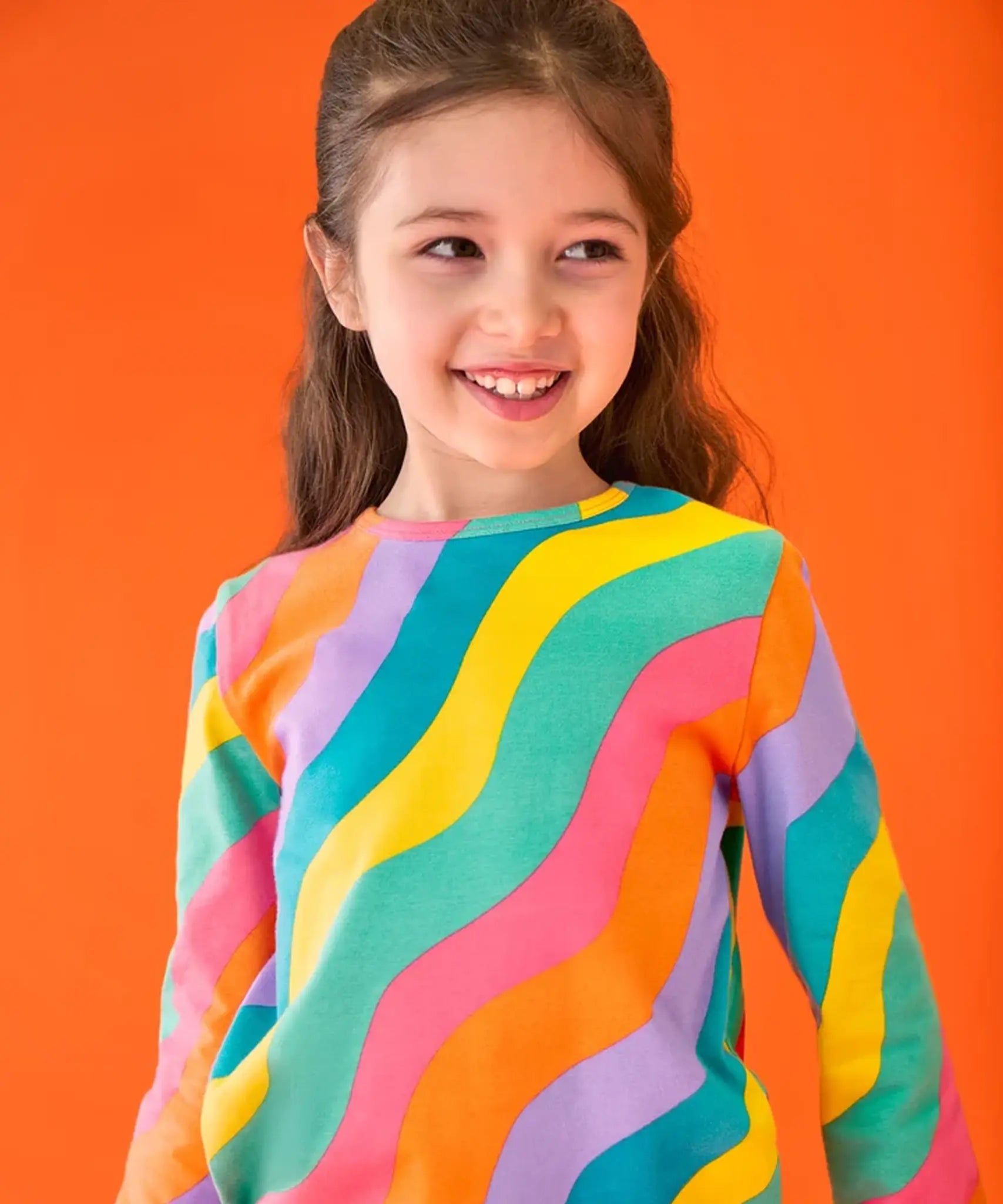Close up of child wearing the Frugi GOTS organic cotton long sleeved sofia skater dress with a rainbow ric rac pattern.