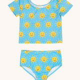 Frugi blue children's tankini with an all over yellow smiley sunshine print. A short sleeved swimwear top with matching brief style bottoms.