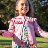 A child wearing the Frugi pink marl Romi cardigan with a matching skater dress. Both the cardigan and dress are made with organic cotton and are a part of a wide range of children's clothing available at Babipur. 