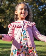 A child wearing the Frugi pink marl Romi cardigan with a matching skater dress. Both the cardigan and dress are made with organic cotton and are a part of a wide range of children's clothing available at Babipur. 