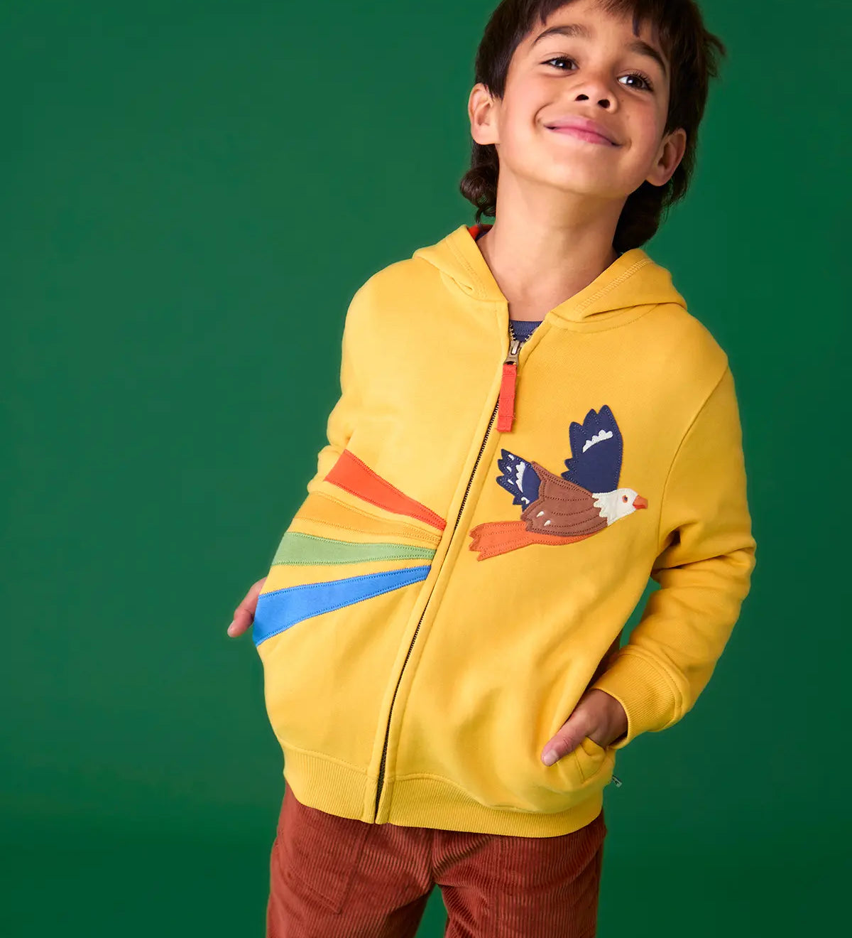 Child wearing the Frugi organic cotton blaire zip hoodie in bumblebee yellow with eagle applique with rust brown trousers. 