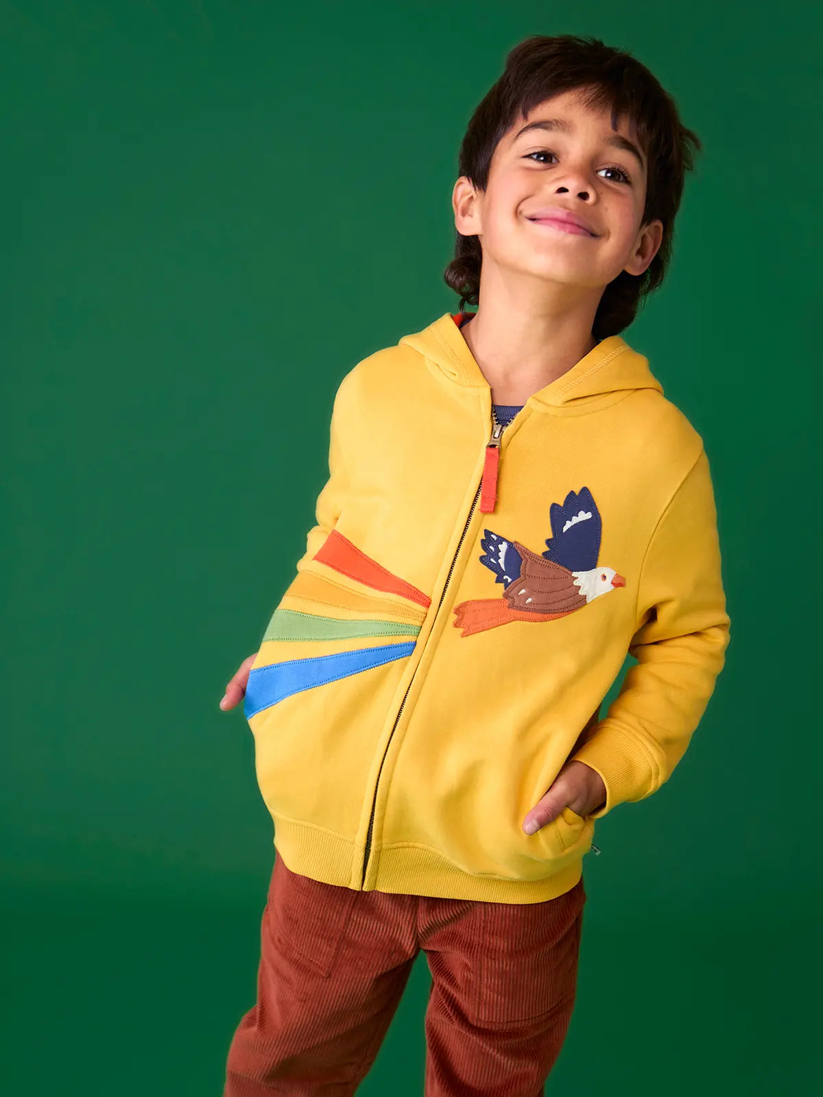 Child wearing the Frugi organic cotton blaire zip hoodie in bumblebee yellow with eagle applique with rust brown trousers. 