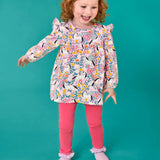 Child wearing the Frugi organic cotton Charlotte outfit. All over floral flight, frilled shoulder long sleeve top with rhubarb pink leggings.
