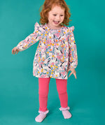 Child wearing the Frugi organic cotton Charlotte outfit. All over floral flight, frilled shoulder long sleeve top with rhubarb pink leggings.