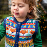 Child wearing the Frugi fox fair isle organic cotton wenn knitted waistcoat. Multi-coloured fair isle knit with navy edges and wooden buttons with a long sleeved green top underneath.