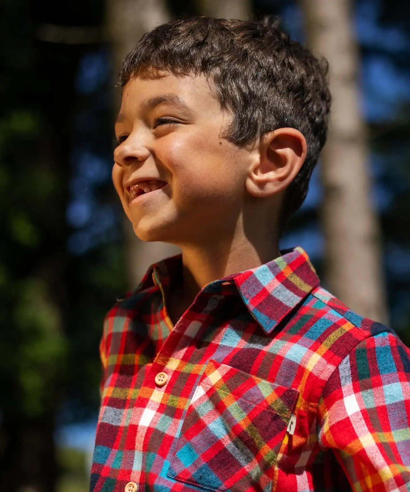 Child wearing the Frugi organic cotton festive check hector long sleeve shirt with chest pocket. Close up of collar.