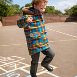 Child wearing Frugi's Penhale parka coat in a blue red and yellow tartan check with the faux fur trimmed hood down playing hopscotch in a playground.
