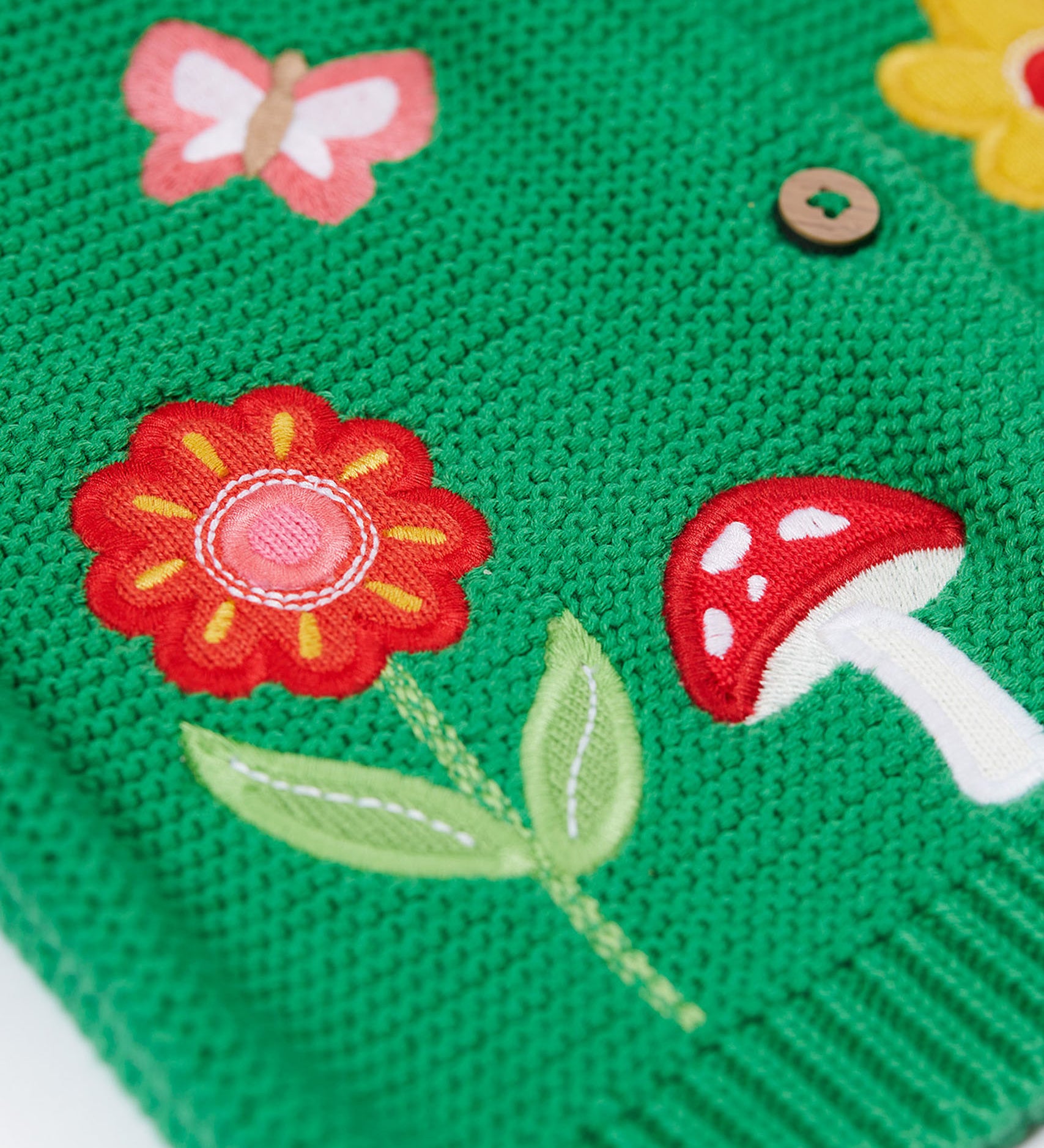 A close up of the flower and mushroom appliques on the front of the Frugi colby clover green coloured knitted organic cotton cardigan.