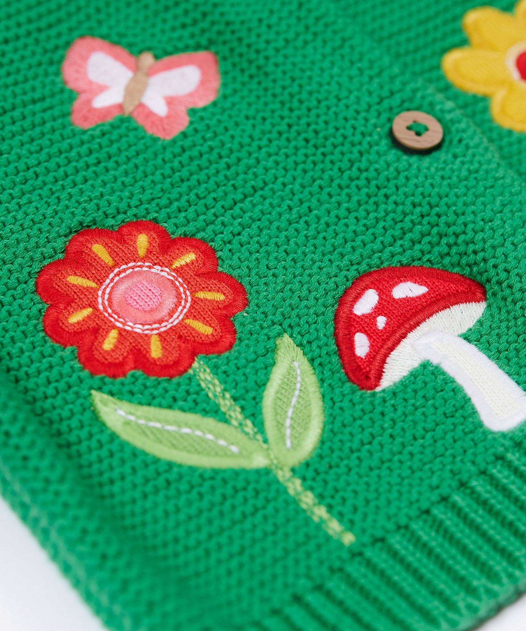 A close up of the flower and mushroom appliques on the front of the Frugi colby clover green coloured knitted organic cotton cardigan.
