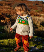 Child wearing Frugi clyde cable knit organic cotton jumper natural highlands cow and puffin design with rust highland cow corduroy trousers.
