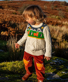 Child wearing Frugi clyde cable knit organic cotton jumper natural highlands cow and puffin design with rust highland cow corduroy trousers.