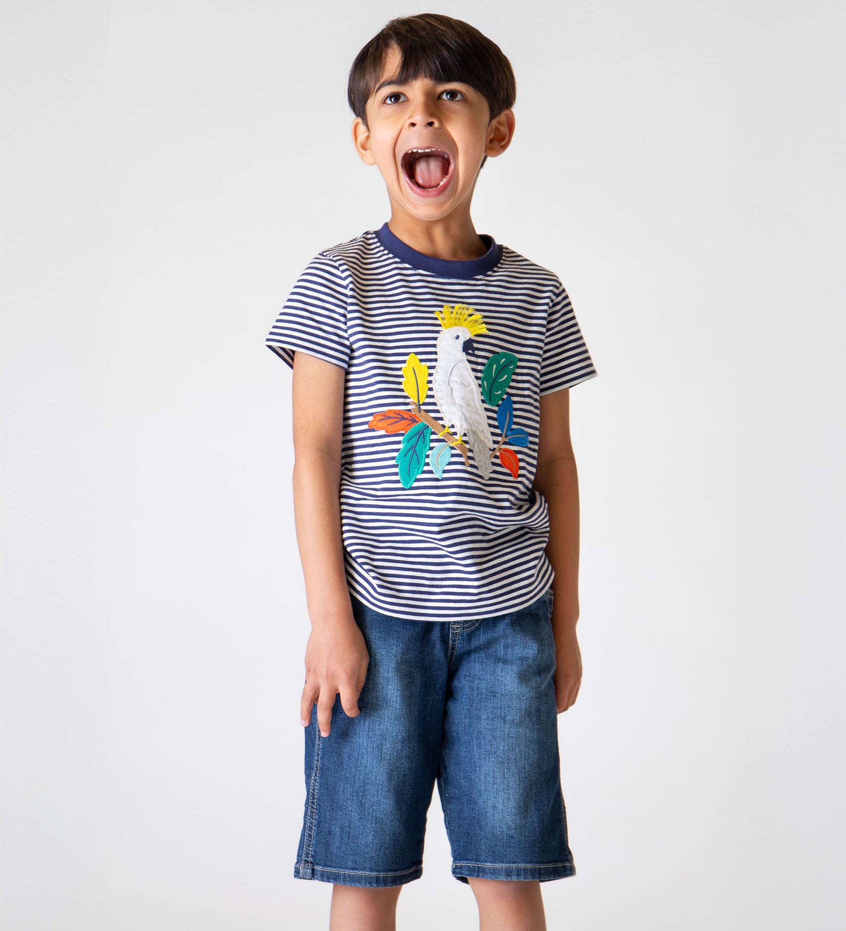 A child wearing the Frugi Elijah Applique T-Shirt - Navy Stripe / Cockatoo with denim shorts.