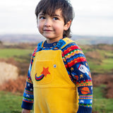 Child wearing the Frugi Gylly cord reversible dungaree in bumblebee yellow with star pocket design with a fair isle knitted jumper underneath. 