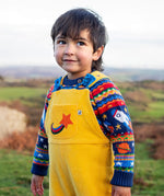 Child wearing the Frugi Gylly cord reversible dungaree in bumblebee yellow with star pocket design with a fair isle knitted jumper underneath. 