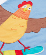 Close up of the Frugi kids cornflower blue chicken t-shirt. Showing the appliqué detail of a brown chicken standing on a skateboard on light blue organic cotton fabric