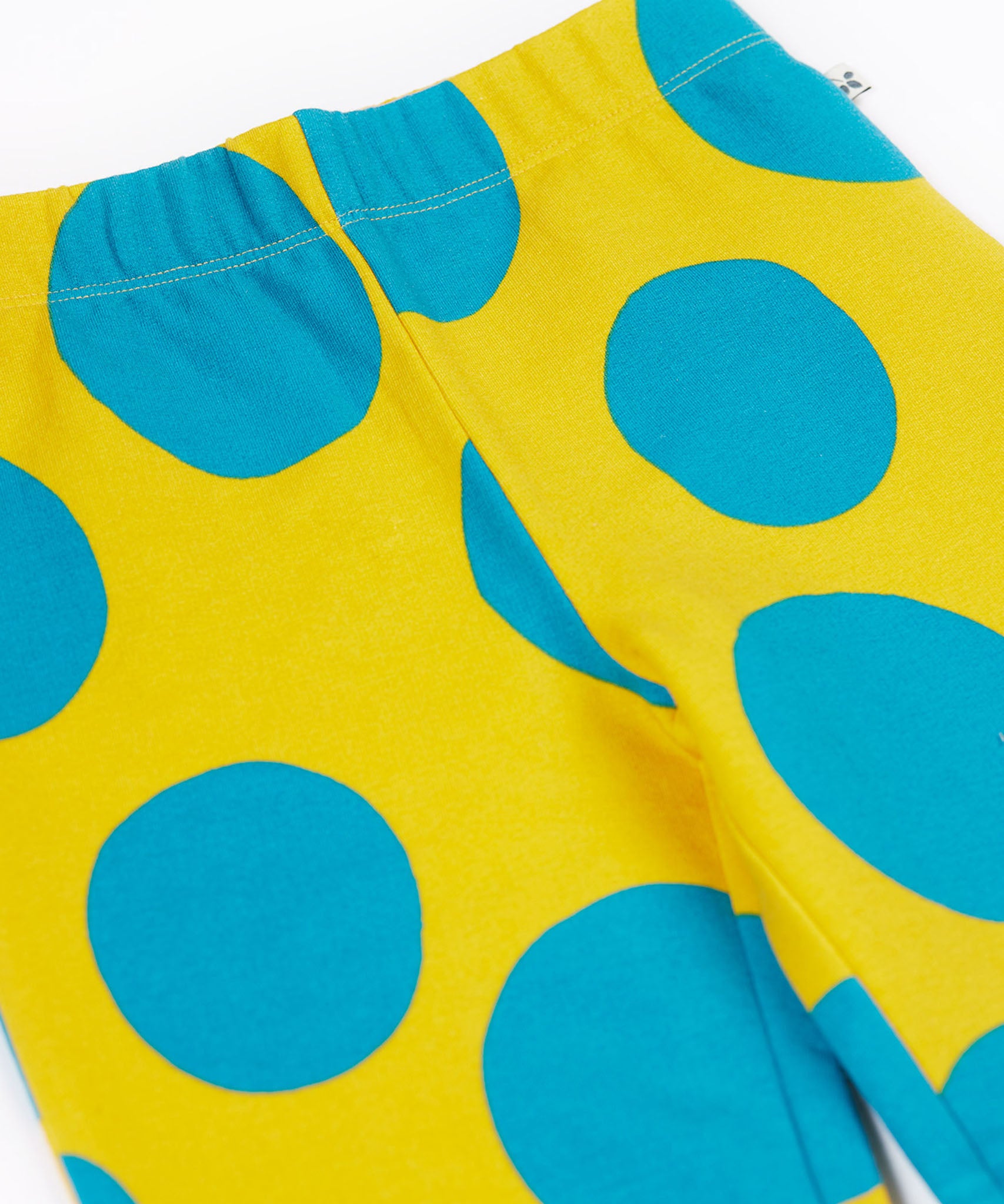 A close up of the Frugi kids cosy flared leggings in super spot showing the bold blue spot design on yellow organic cotton fabric.