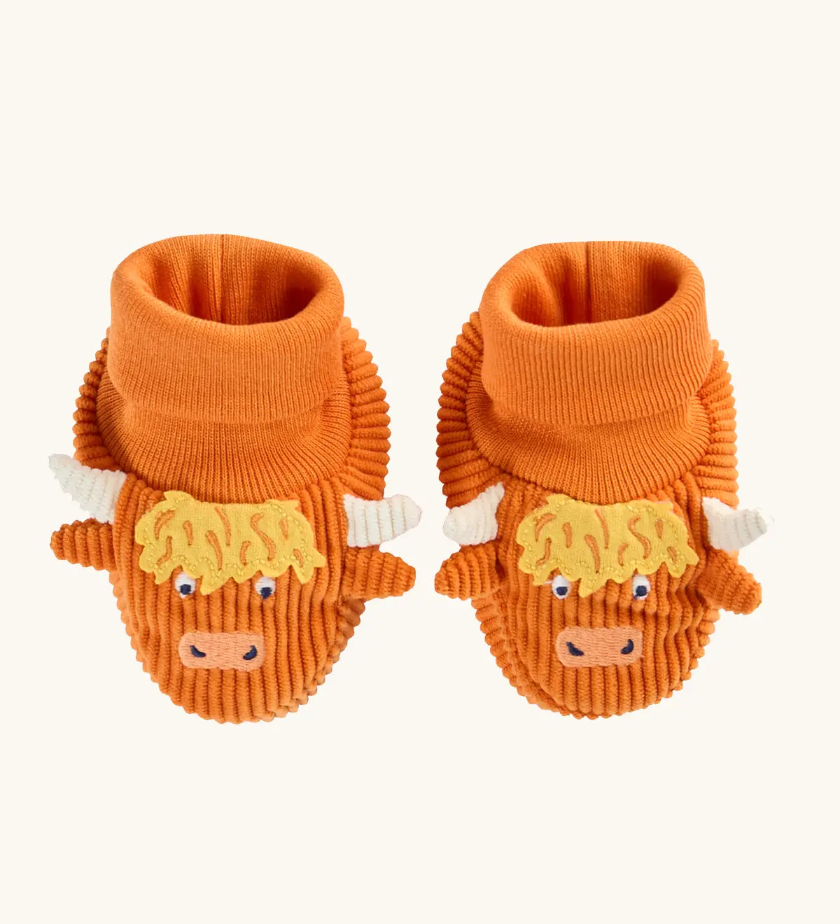 A pair of frugi orange corduroy baby booties designed to look like Highland cows, featuring yellow shaggy hair, white horns, and embroidered cow faces.