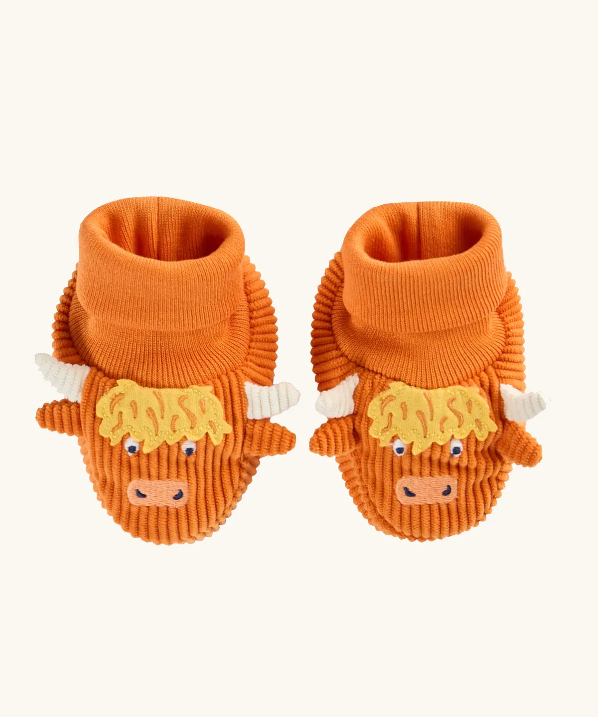 A pair of frugi orange corduroy baby booties designed to look like Highland cows, featuring yellow shaggy hair, white horns, and embroidered cow faces.