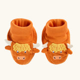 A pair of frugi orange corduroy baby booties designed to look like Highland cows, featuring yellow shaggy hair, white horns, and embroidered cow faces.